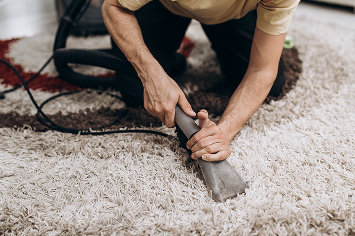 A man carefully hand cleans an area shag rug with a steam cleaner 